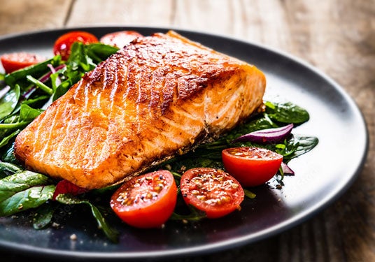 A plate of salmon, baby tomatoes, kale and spinach.