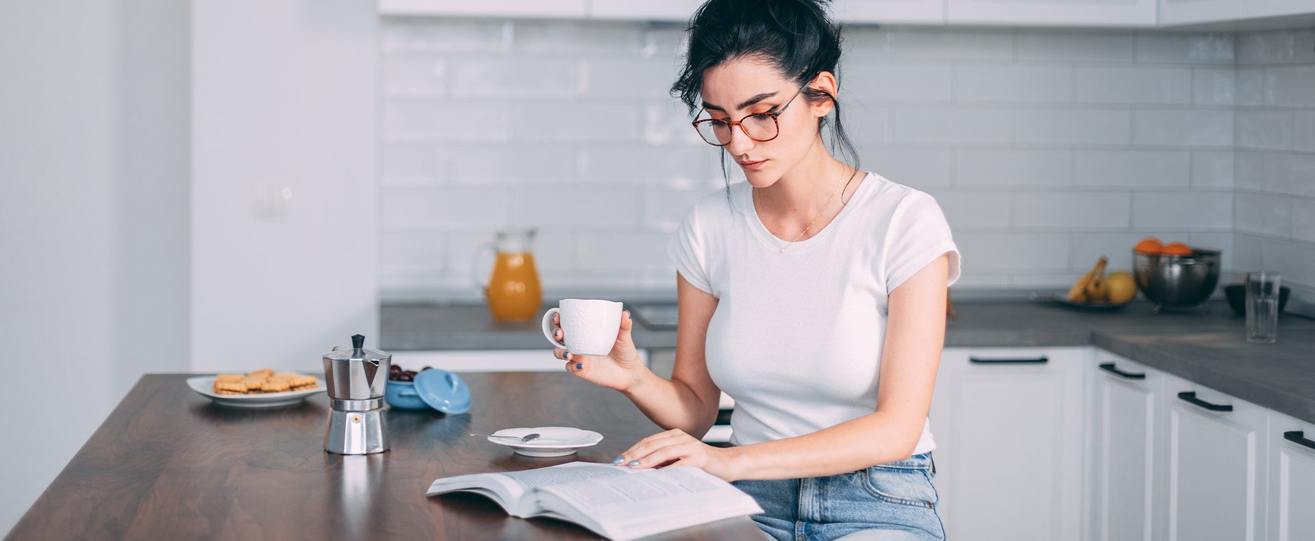 Woman drinking coffee and reading a book in the kitchen
