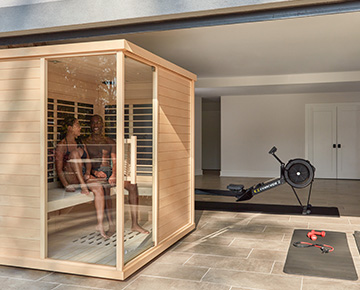 A couple relaxes in a Sunlighten mPulse Discover infrared sauna in their home gym.
