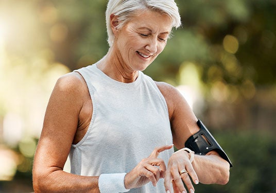An older person pauses from their jog to check their biometrics on their smartwatch.