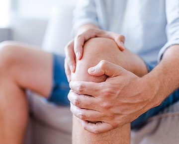 A person seated, holding their knee and leg muscles in pain. 