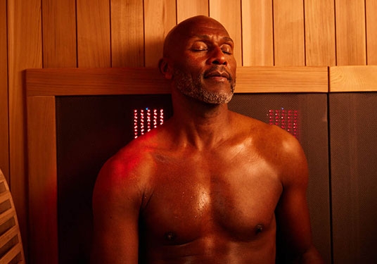 A man rests in a Sunlighten mPulse Smart Sauna, an infrared sauna with red light. 