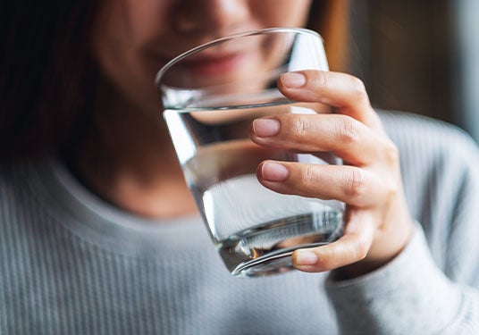 A woman smiling while drinking a glass of water.