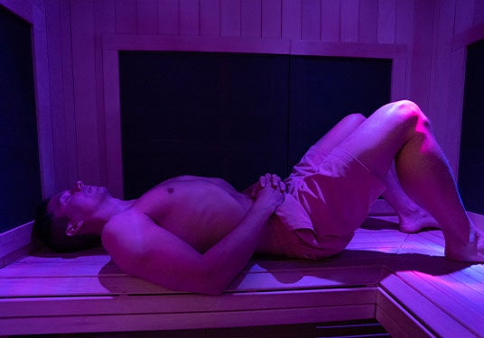man lays on the bench in an infrared sauna relaxing with his eyes closed
