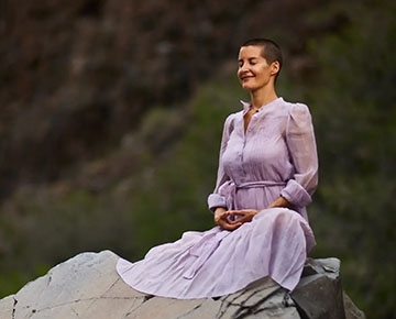 A woman stands peacefully with her eyes closed, enjoying a breeze on a mountain-top 