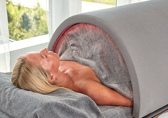 A woman sits in a Sunlighten Solo portable infrared sauna system.
