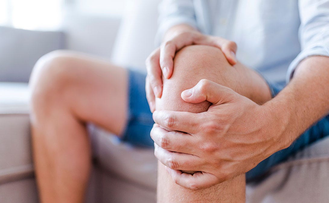 A person seated, holding their knee and leg muscles in pain.