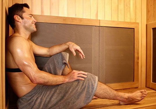 A man sits inside a Sunlighten infrared sauna, smiling and sweating.