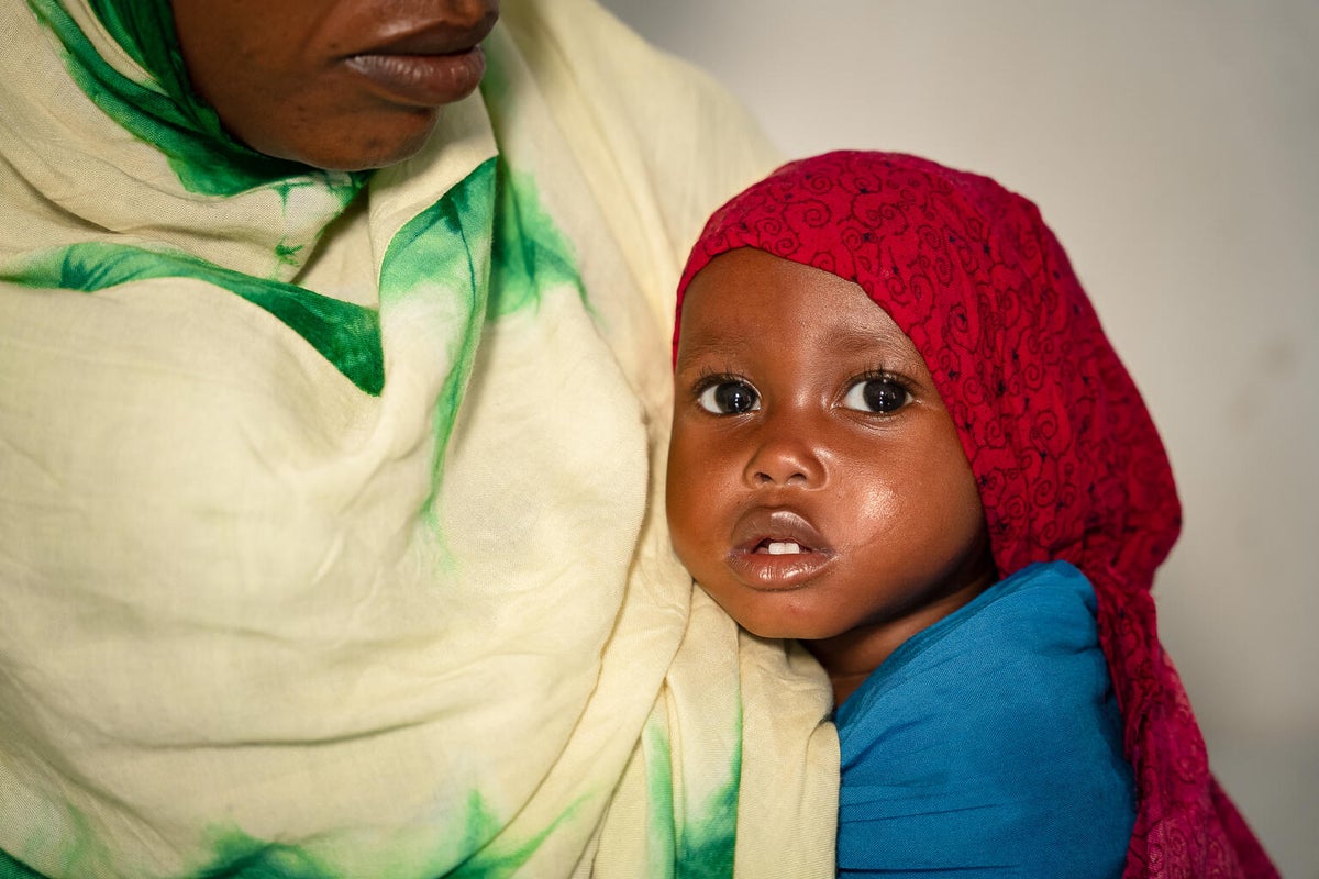 A young baby wearing a red head scarf looks at the camera. 