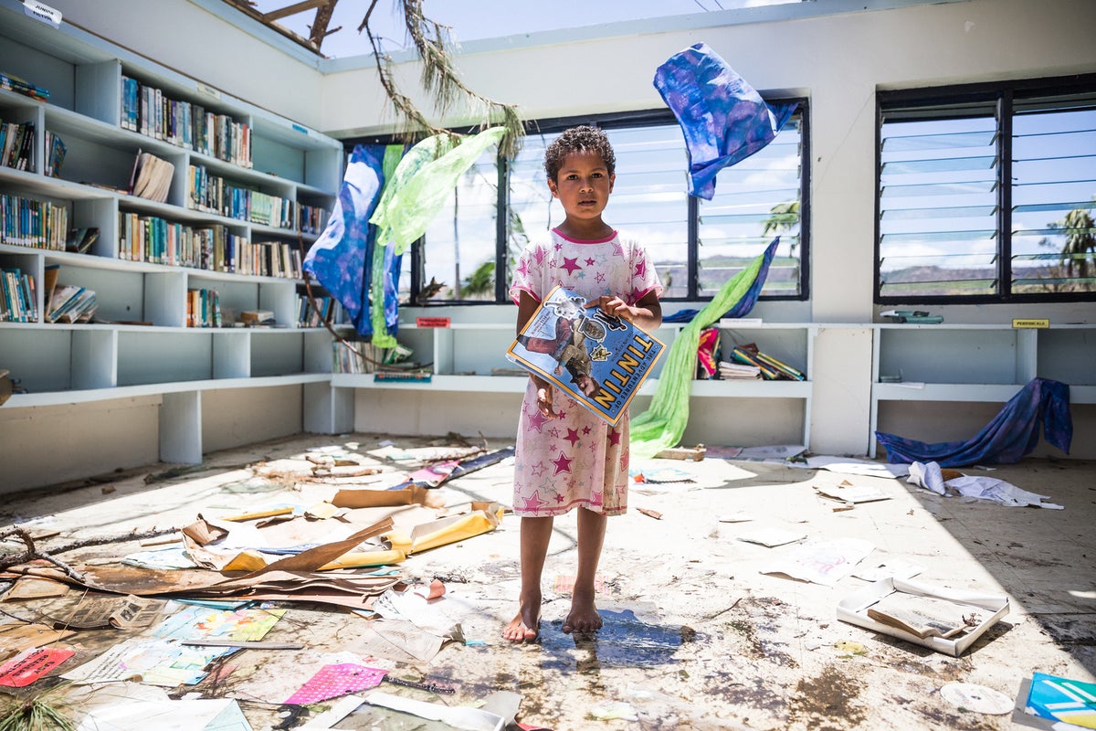 A girl is holding a story book. She is inside a classroom that has no ceiling.