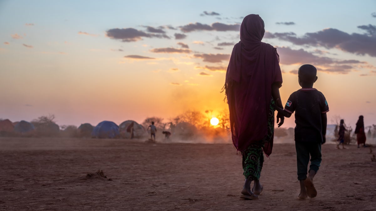 Family walks on dry earth into the sunset