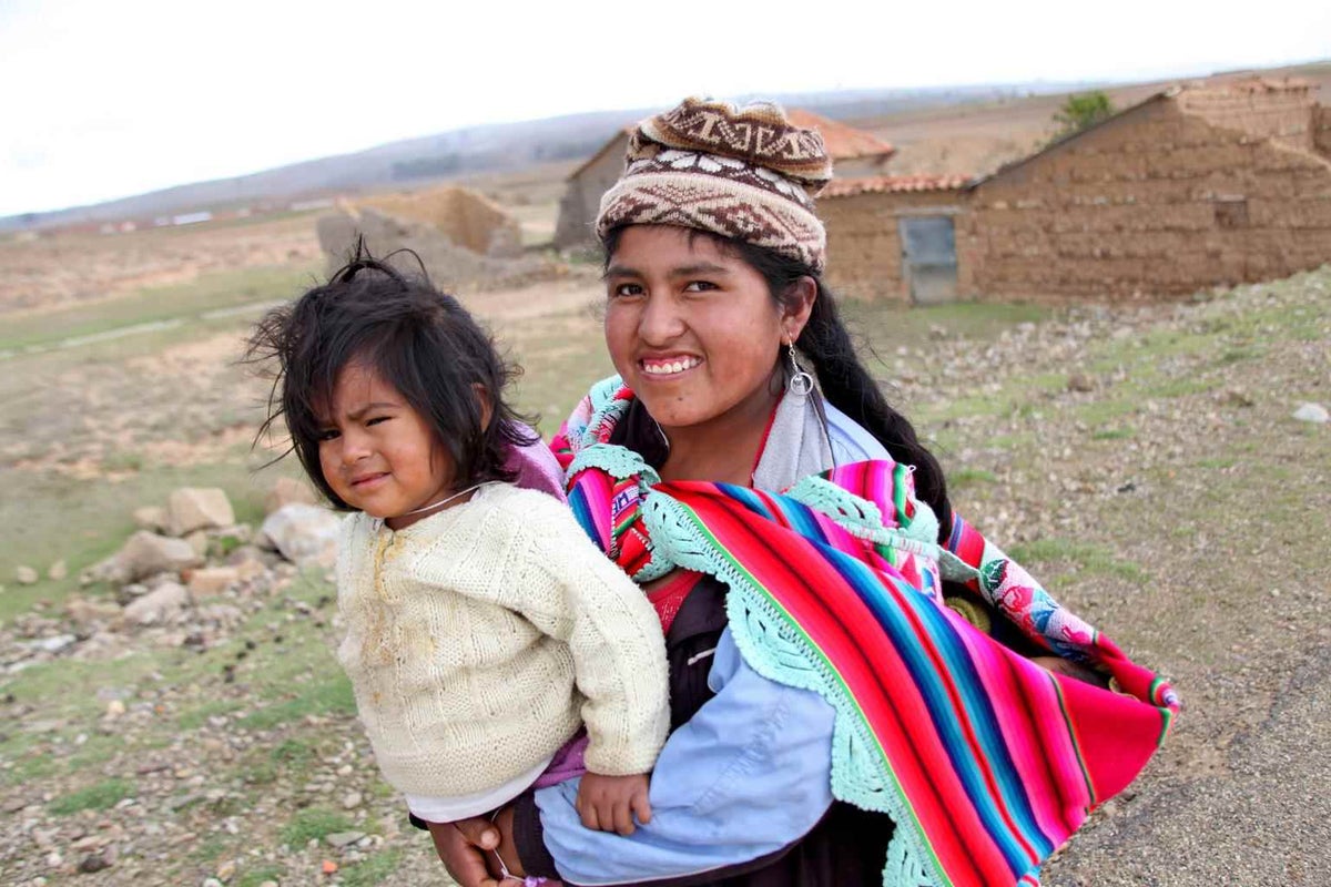 Young mother Melissa carries her daughter Rosa in her arms and baby Daniel in a sling pouch near the capital of Bolivia in 2013. 