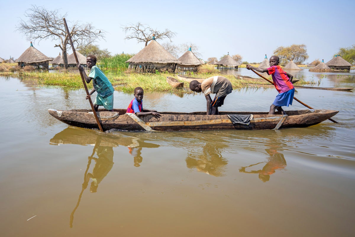 Children canoe past submerged houses in a flooded village in South Sudan