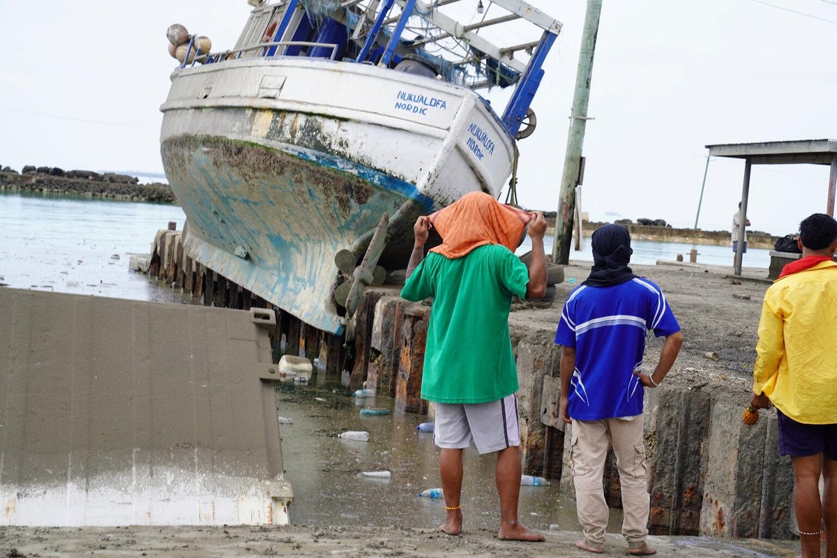 A boat out of the water. Three people are looking at it.