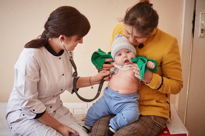 A woman is holding a baby while a doctor does a check on the baby with a stethoscope.