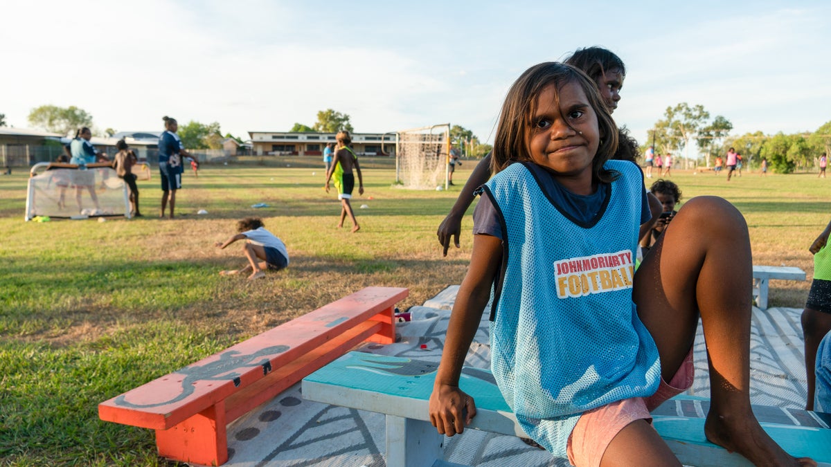 A child sits on a bench and smiles at the camera.