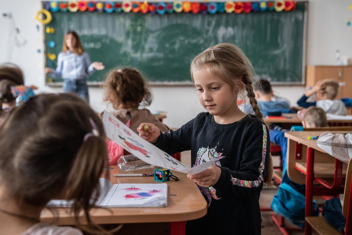 A young Ukraine girl is in a classroom in Romania showing another child her artwork.