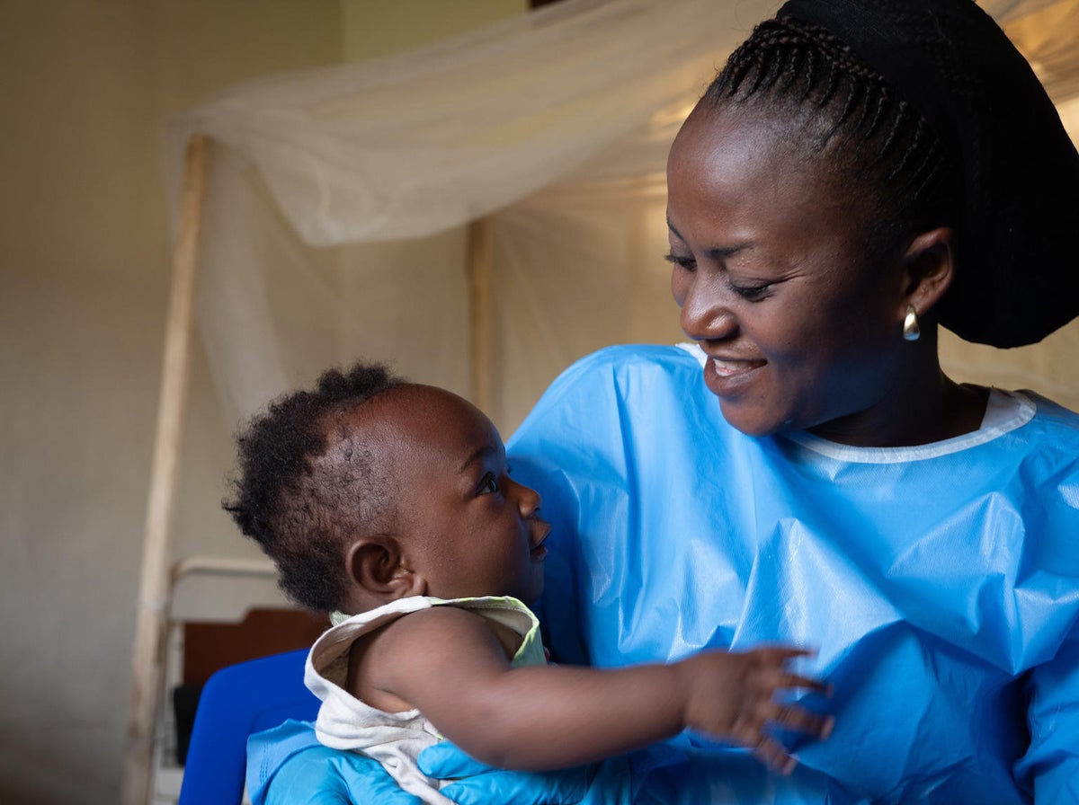 A woman wearing protective gear is holding a baby.