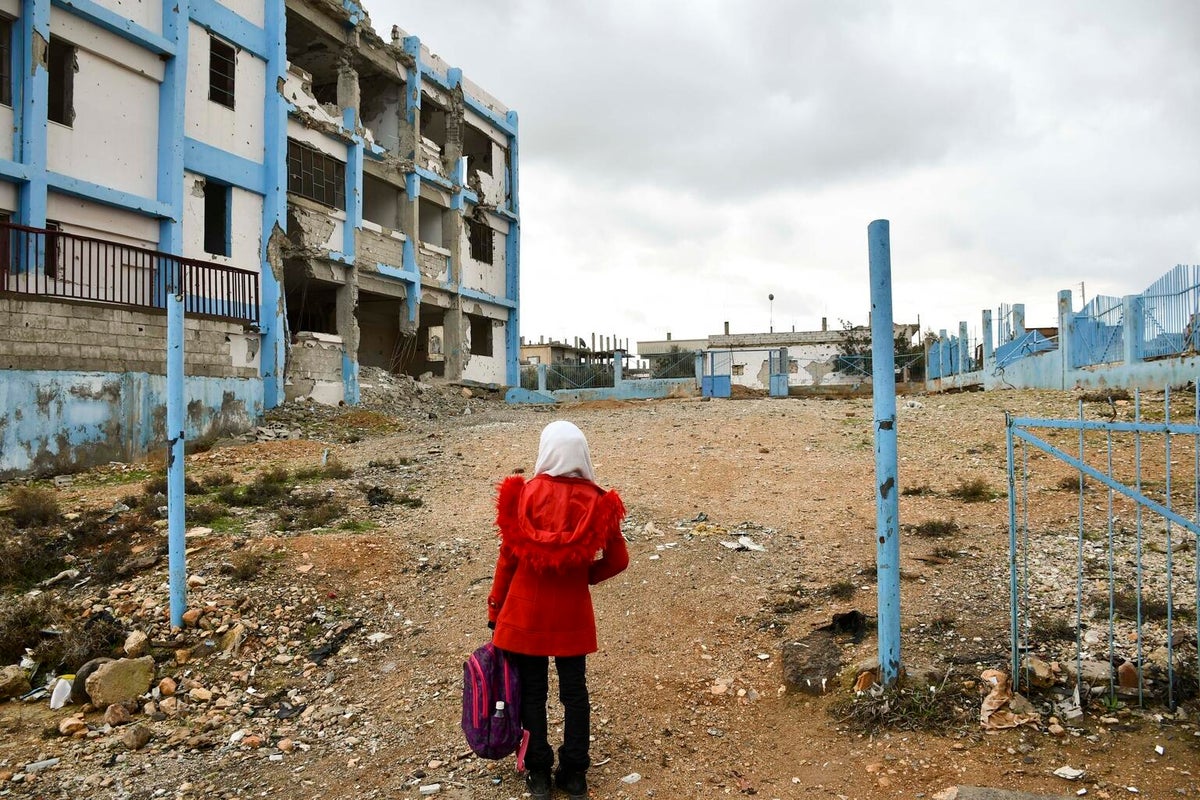 A girl looking at a damaged school. 