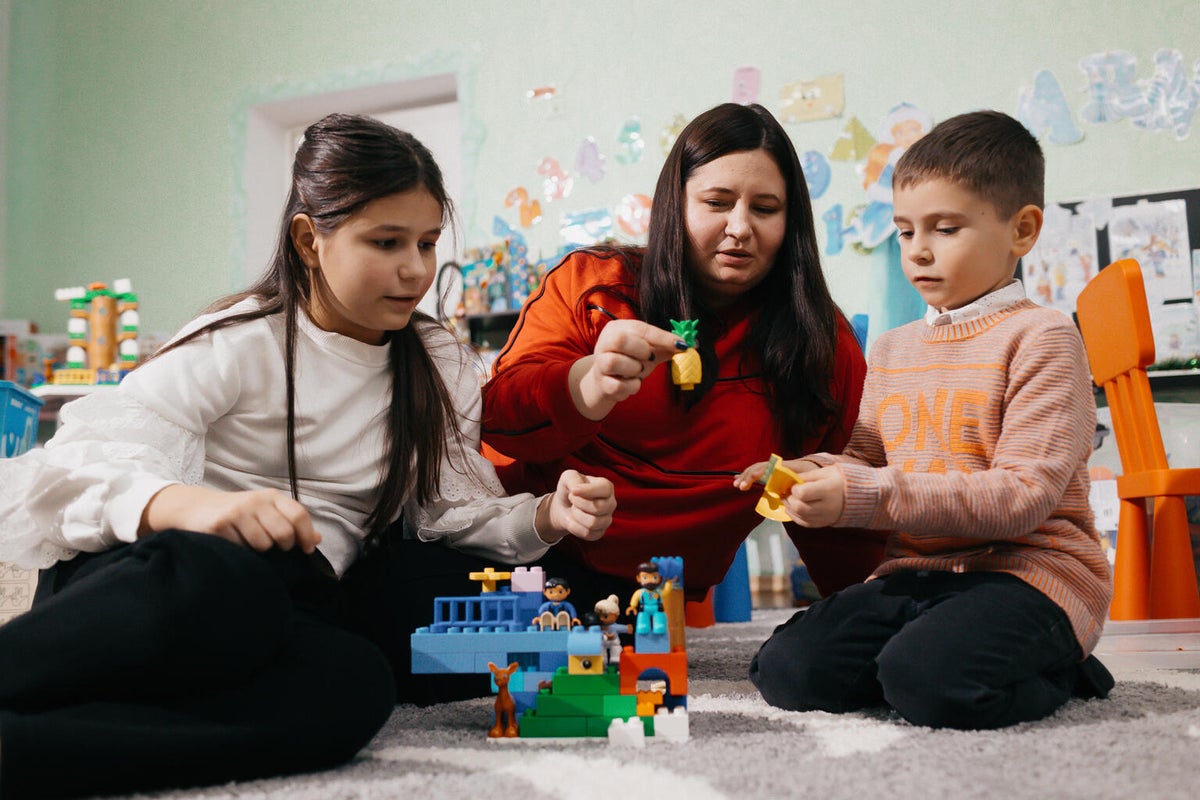 A mother and her two young children play with LEGO blocks