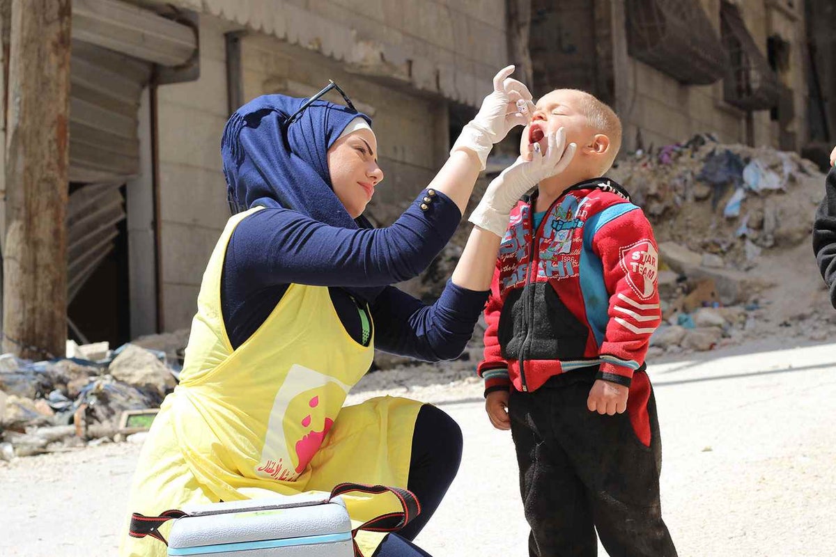 Woman dropping polio vaccine into the mouth of a child