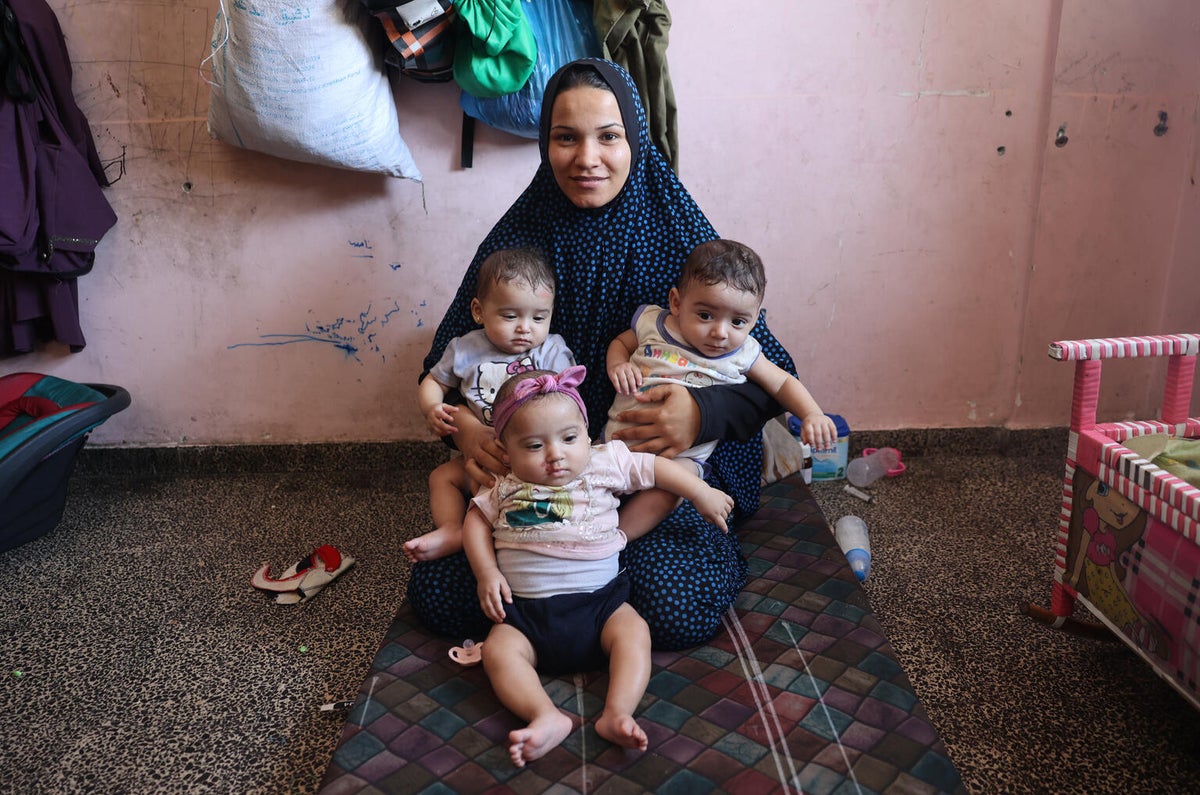 A mother holds three infant children at a UNICEF-supported paediatrician clinic in the Gaza Strip.