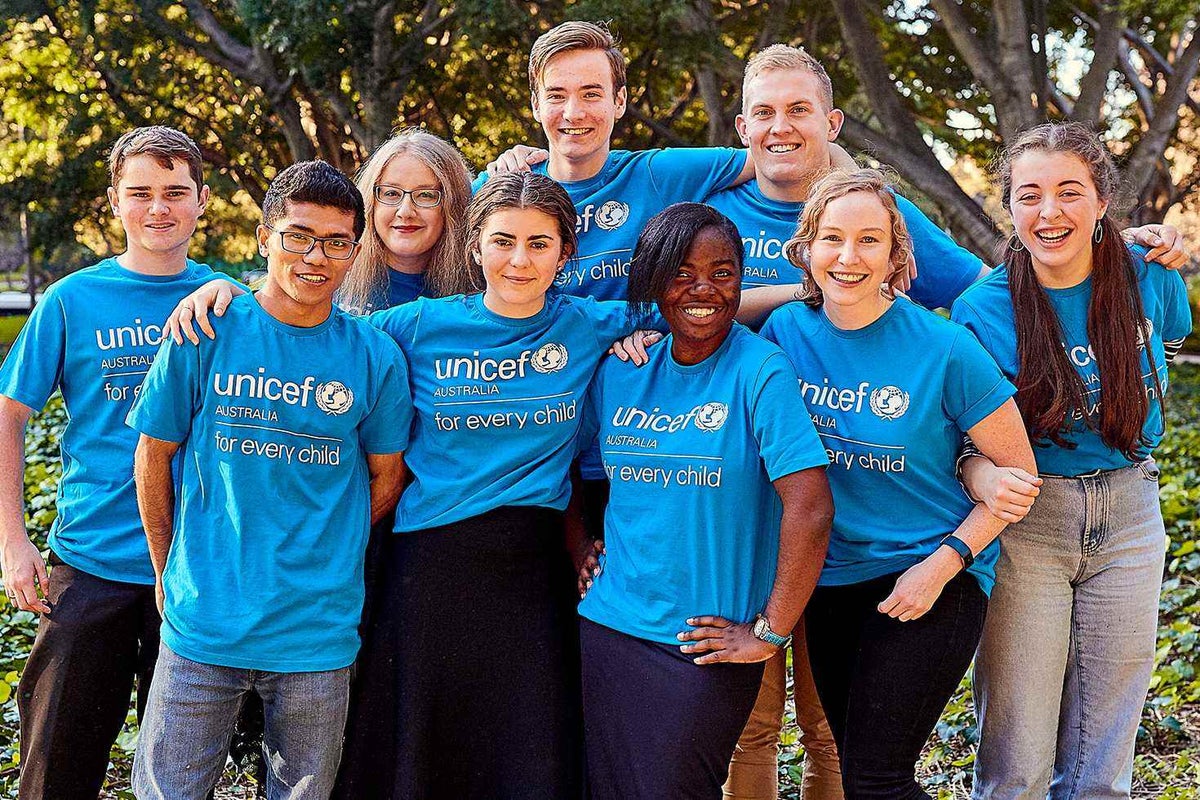 A group of 9 young people wearing UNICEF t-shirts smiling and looking directly into the camera
