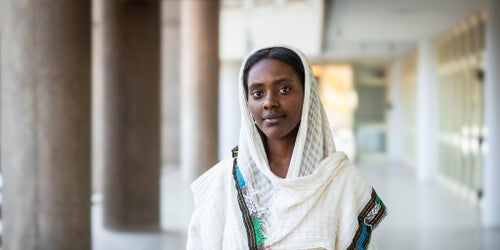 A young Ethiopian woman wearing white looks into the camera as she stands in a spacious area.