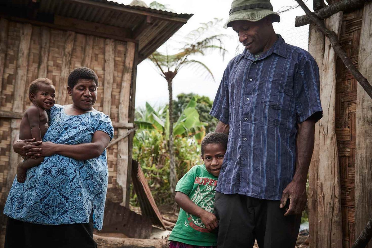 Lucy, 23, holds her daughter Kathy while her husband Palus, 31, stands next to their eldest child Lilian, 6, outside their home in Siure, Chimbu.