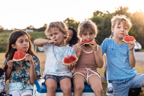 A group of four young children sit and eat watermelon.