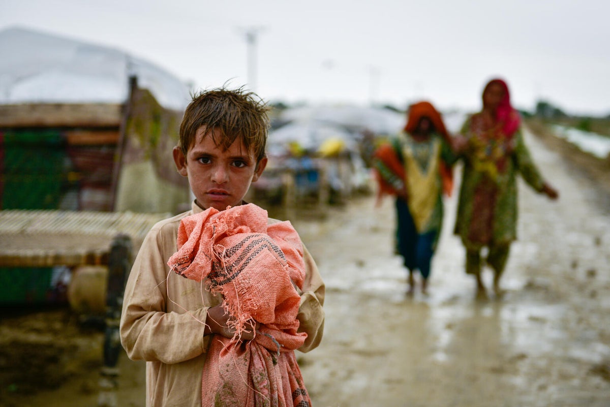 A child holding a package of belongings. He is standing on a dirty road that looks very muddy.