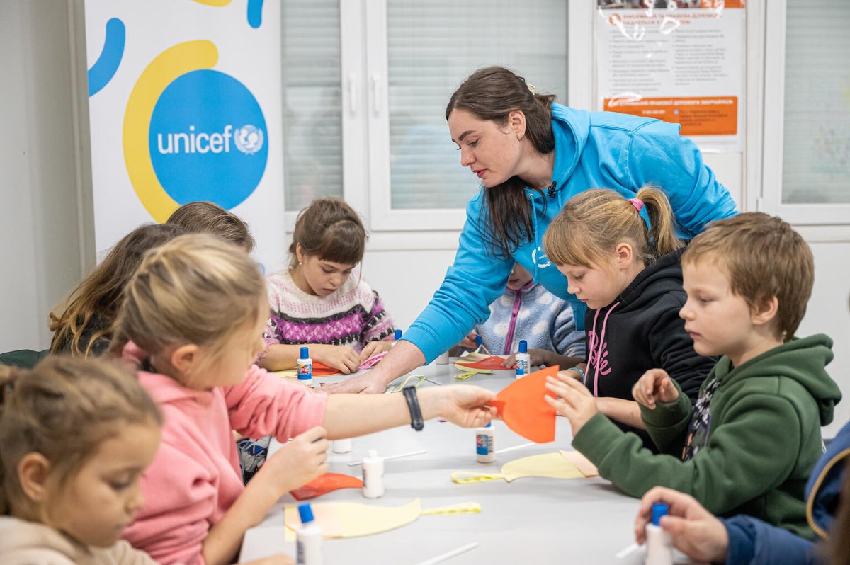 A group of children sitting around a table make Christmas decorations with the help of a social worker wearing a UNICEF jacket