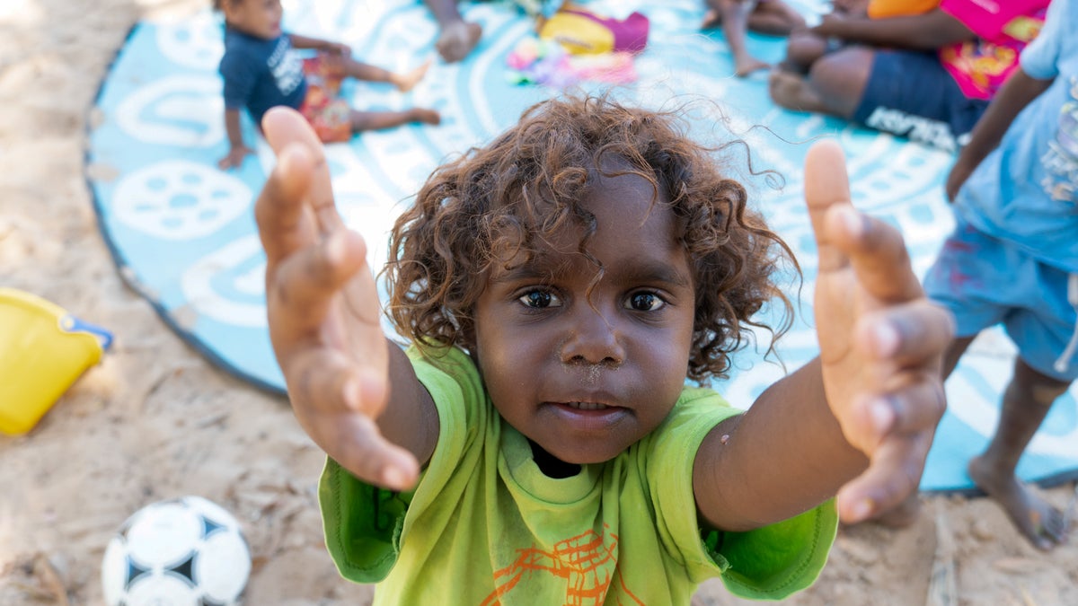 A young child extends his hands towards the camera. 