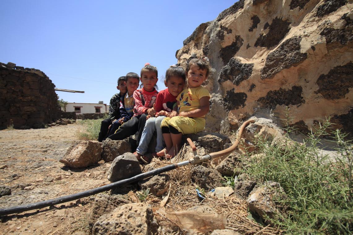 Children sit in front of irrigation in their home town in Syria