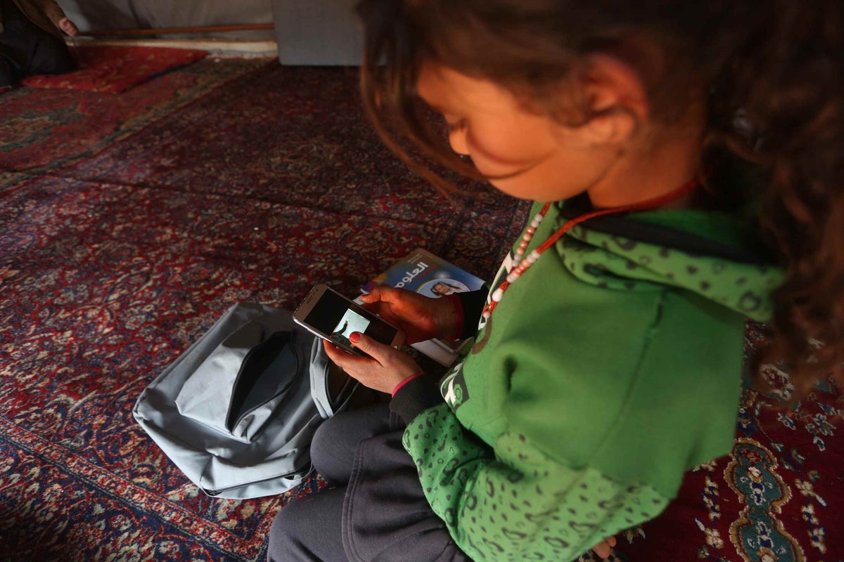 A young girl is looking at the screen of a mobile phone.