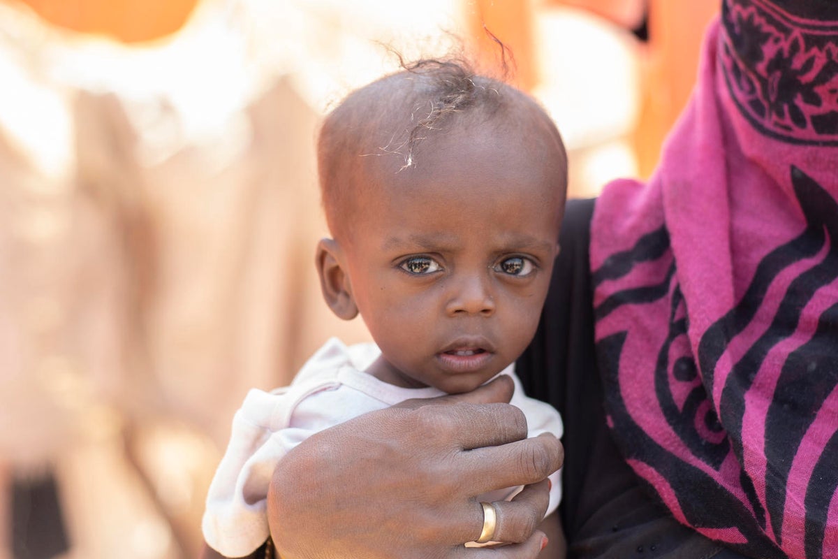 A woman holding a baby. The baby is looking at the camera and he looks upset.