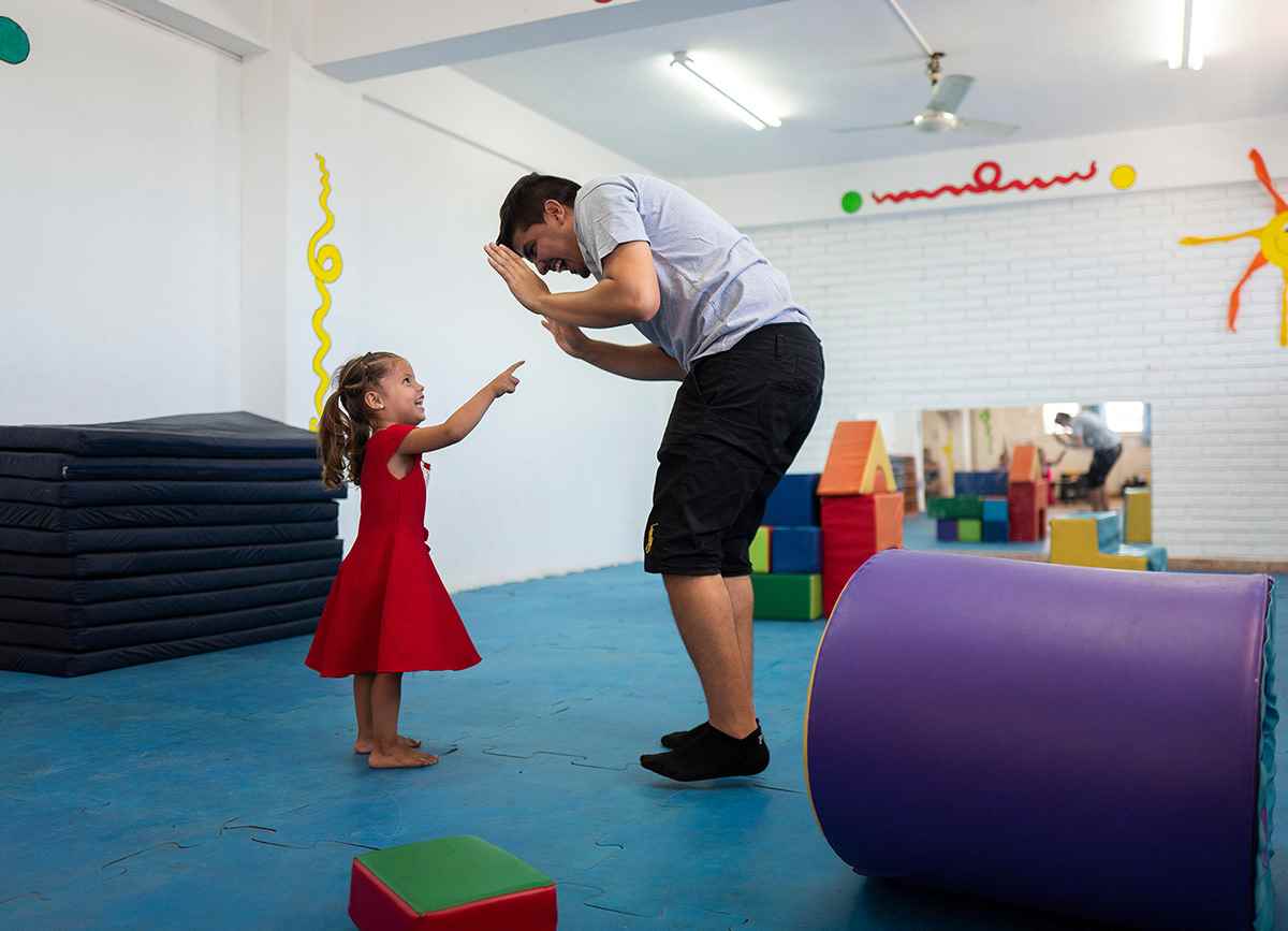 A three-year-old girl happily points at her dad who is playing with her in a play centre.