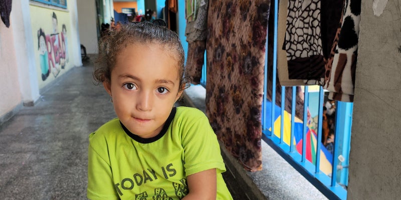 Child in yellow shirt standing in front of classrooms where they are sheltering during the Gaza crisis