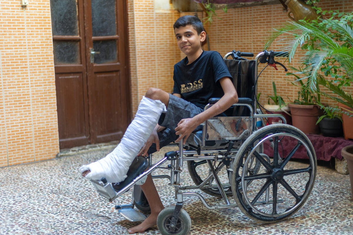 A teenage Syrian boy in a wheelchair with a bandaged leg smiles at the camera