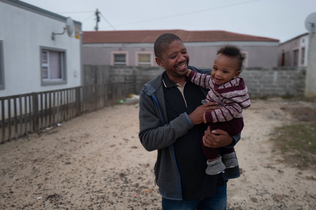 Man holding son while walking in the street.