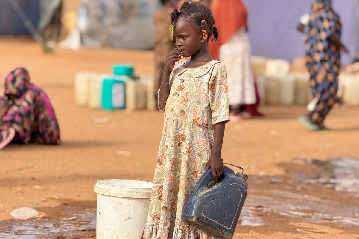 Child queues for water with water containers around her