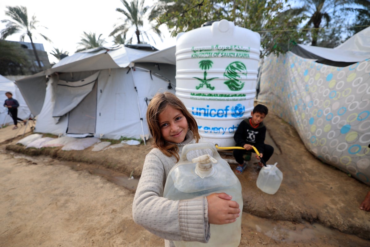 Fatima, 12, smiles as she collects water from a UNICEF-installed tank near her temporary shelter in Gaza.