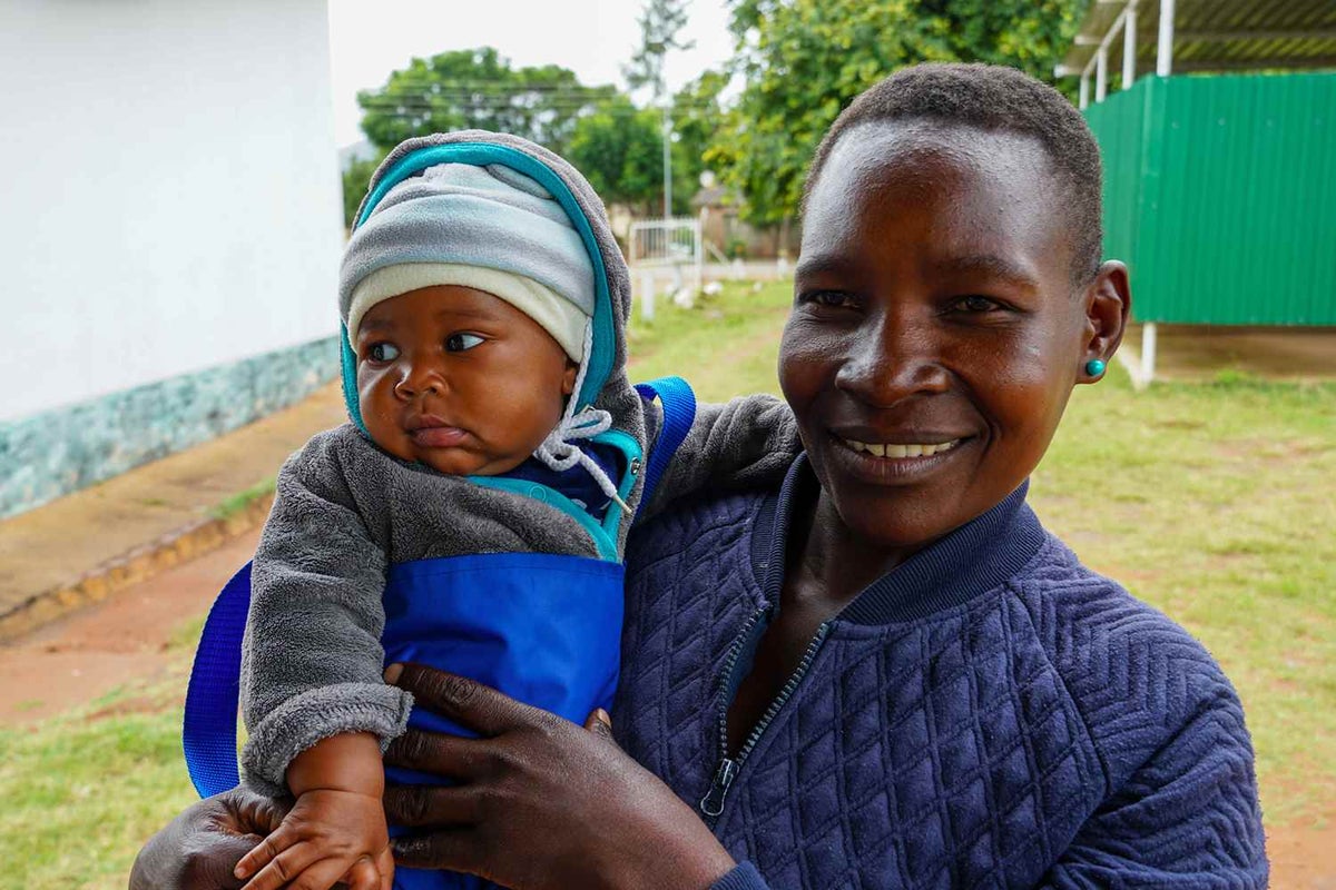 A healthy five-month-old and his mother smile at a UNICEF-supported rural health care clinic. The baby has just been weighed as cleared of malnutrition.