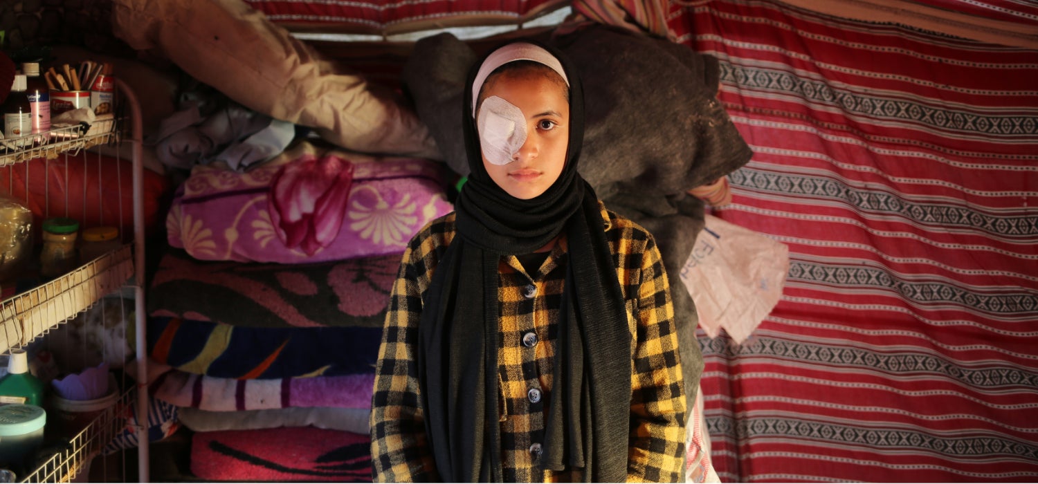 A displaced girl wearing an eye patch after her eye was damaged by shrapnel stands in her tent in the Gaza Strip.
