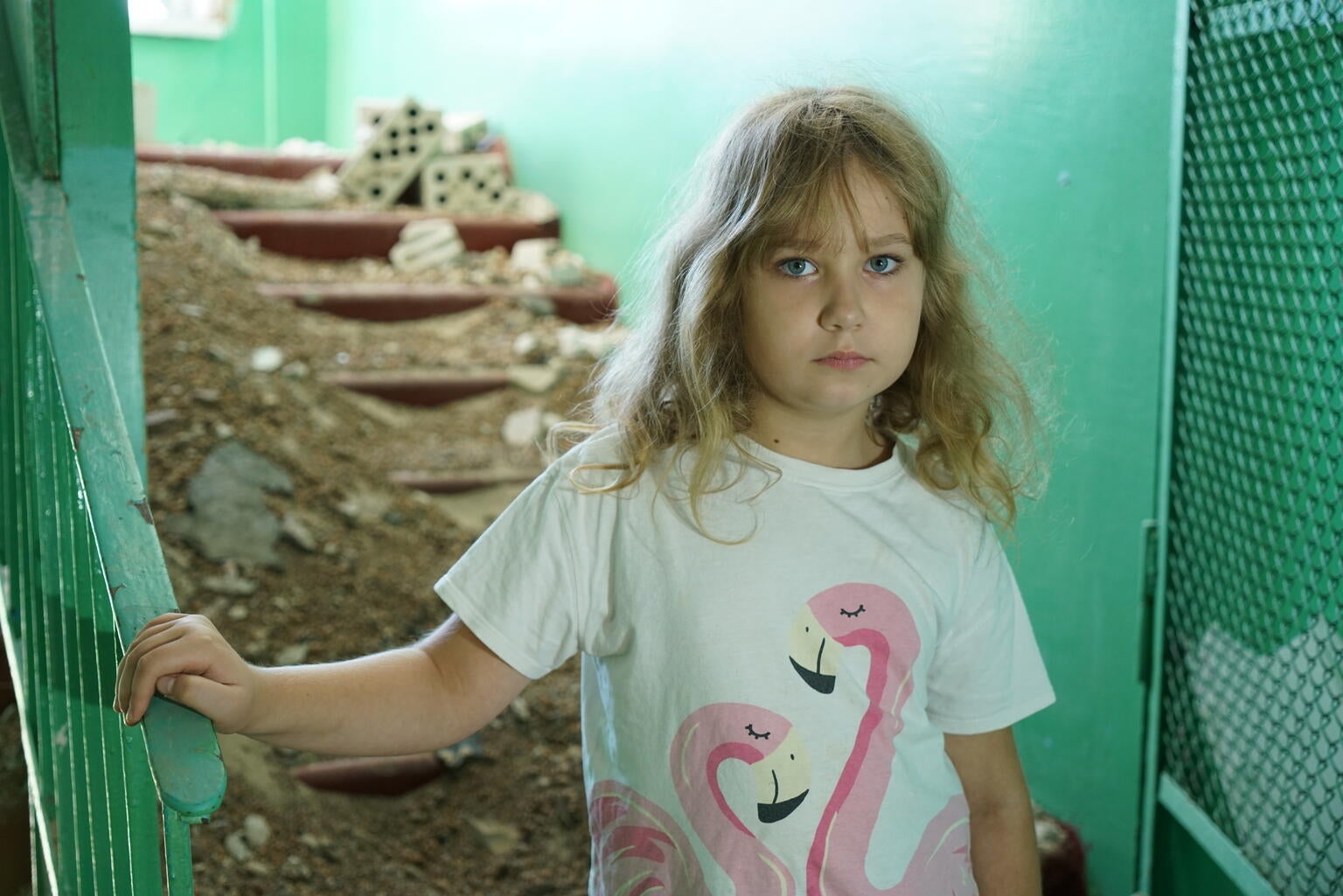 A girl looks at the camera in front of a pile of rubble that used to be her school.
