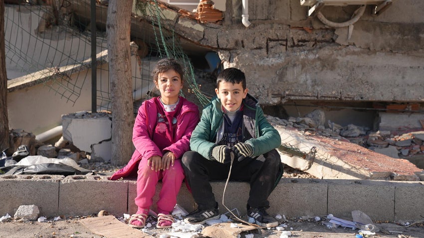 Two young kids in Türkiye sitting out the front of rubble. 