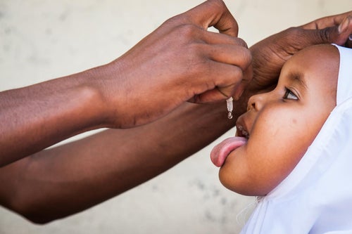 A young girls receives a droplet vaccine from a health worker