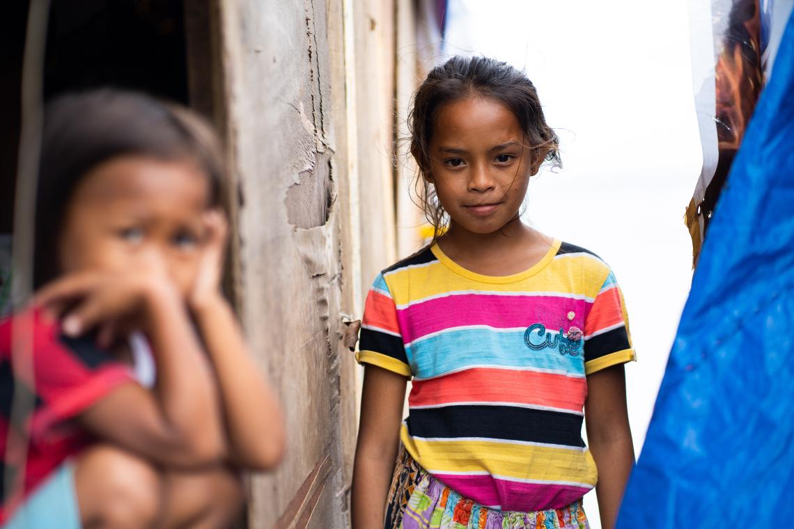 Child smiles looking at the camera, standing between makeshift tents