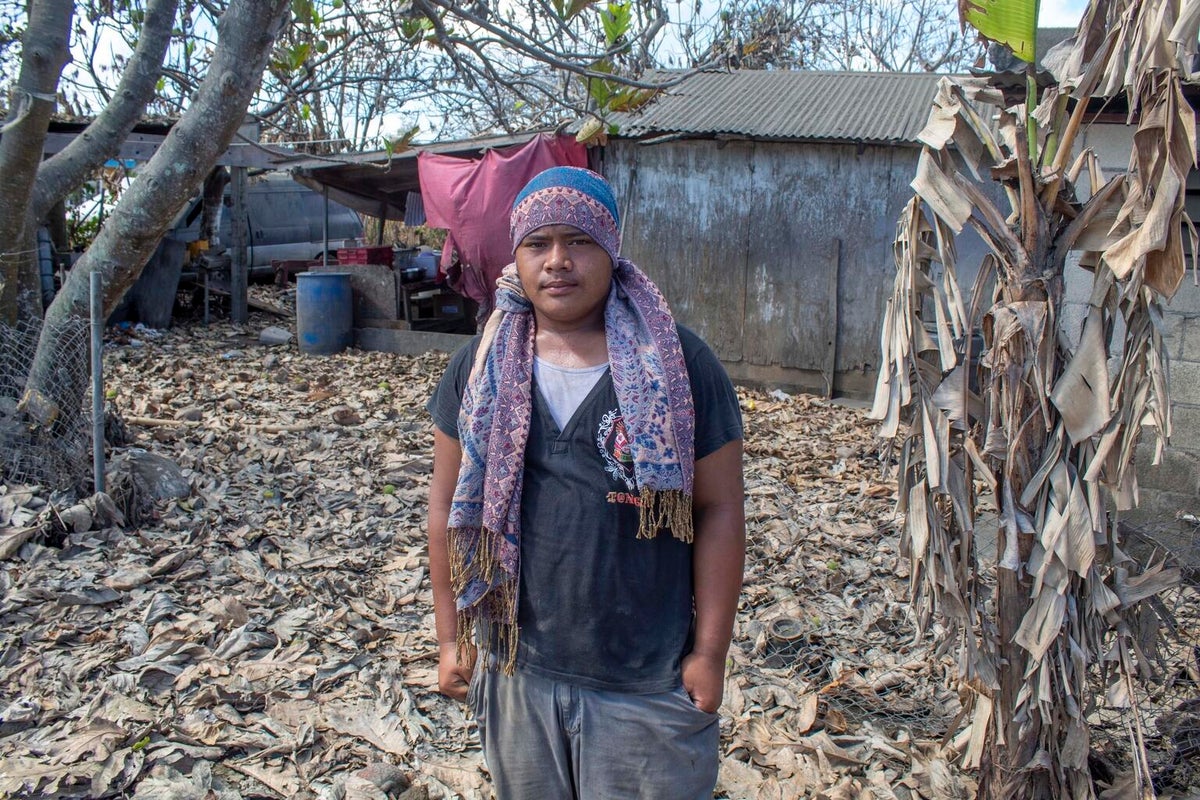 A young man looking at the camera. Behind him, it's all full of tsunami debris.