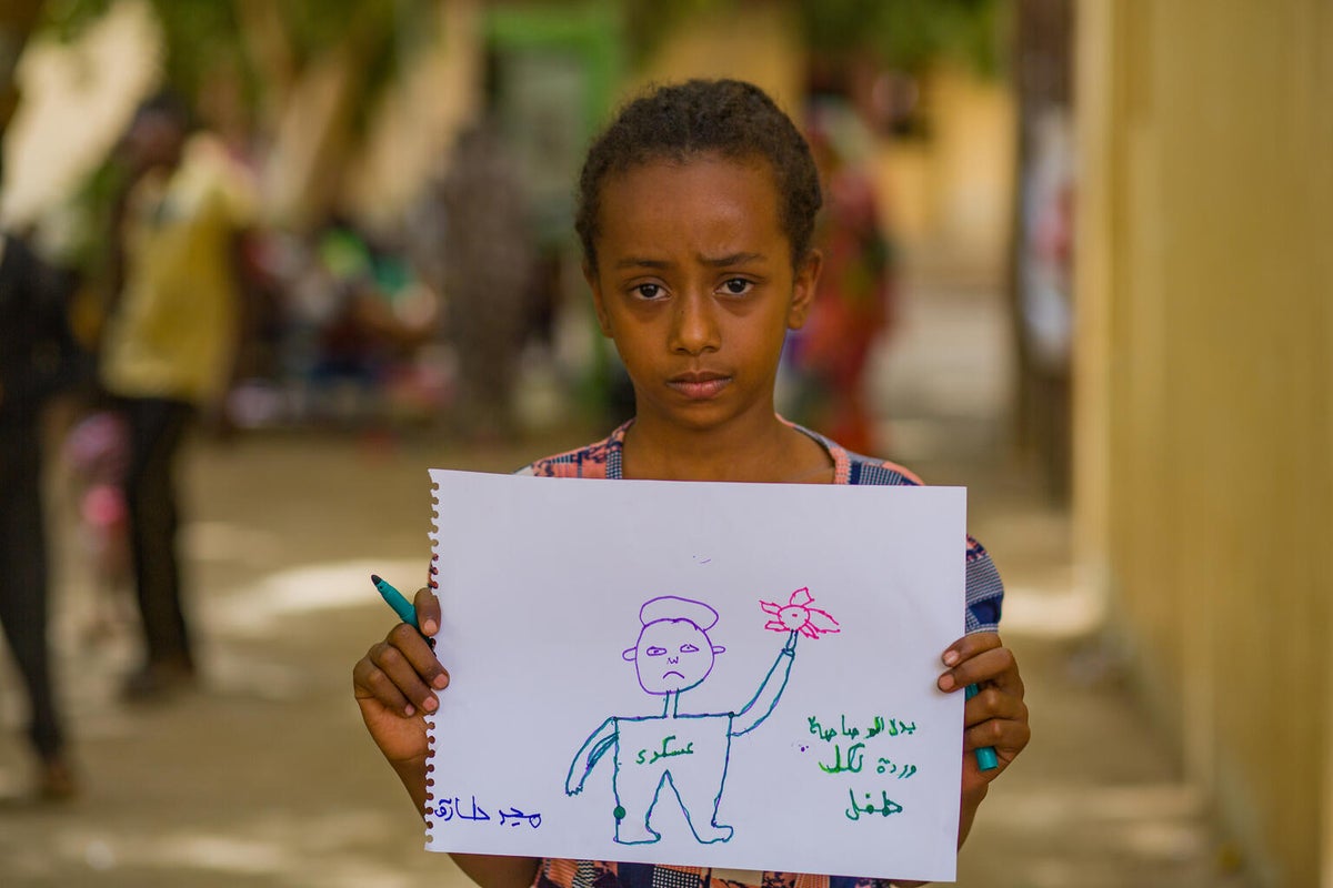 A young girl holds up her drawing of a person holding a rose 